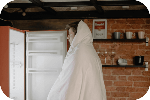 Un homme se tient debout devant son frigo il est recouvert d'une couverture
